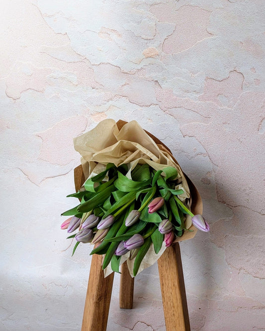 Elegant bouquet of pastel tulips wrapped in brown paper, resting on a wooden stool, handcrafted by Umasari Florist in Thornbury, Melbourne. Ideal for special occasions, corporate gifts, or home decor in Melbourne’s northern suburbs