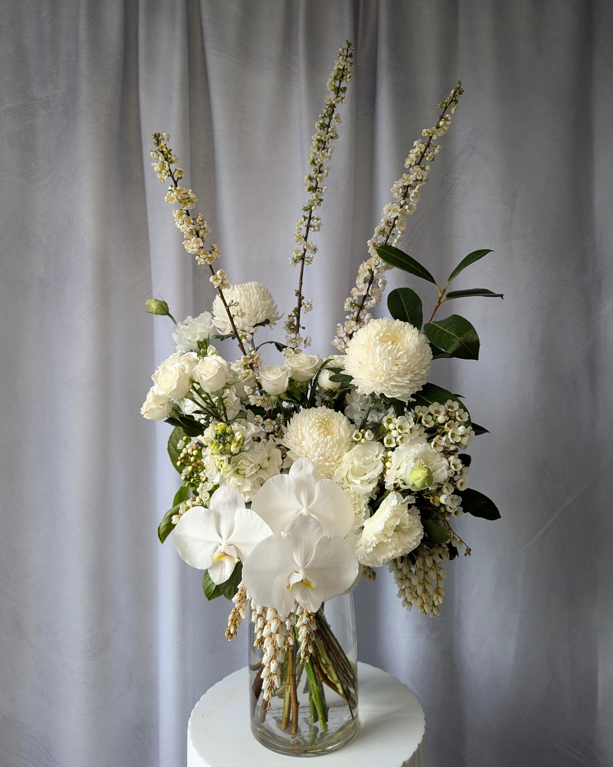 Bouquet of white flowers in a clear vase on a grey background for delivery in Melbourne. Perfect for a sympathy bouquet. 